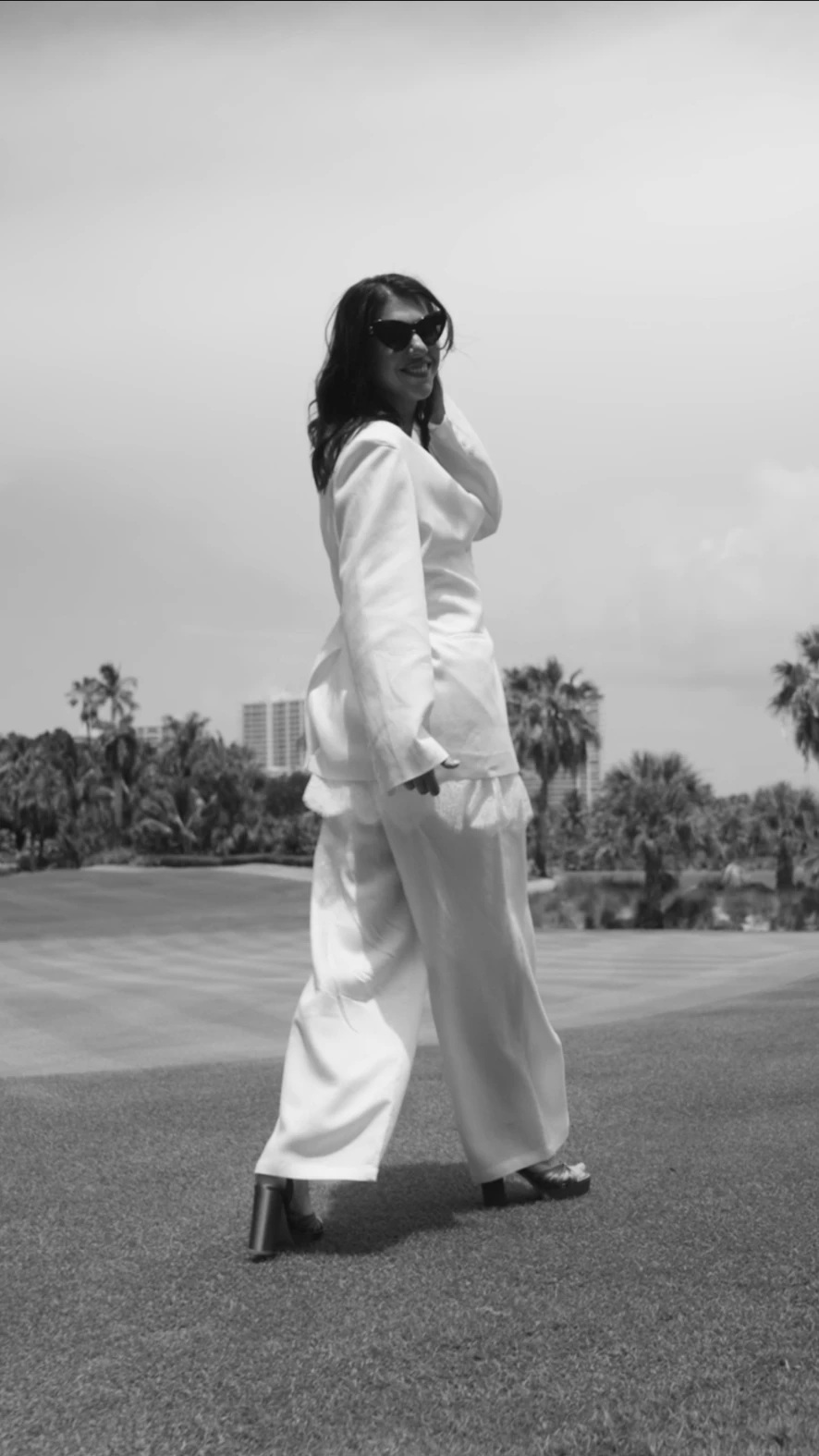 Maria Cristina Banu in a white suit, walking in a palm-lined landscape